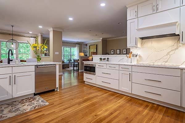 Leo Lantz Construction kitchen remodeling view 2 White kitchen cabinets with honey colored floor and stainless steel appliances looking through to a family room and a wall of windows